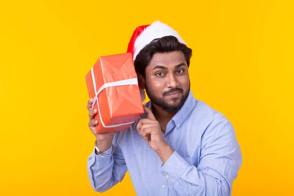 Pozitív fiatal indián férfi Mikulás ajándékokat és karácsonyfát jelentő a sárga háttér. Karácsonyi és újévi ünnepek koncepció. — Stock Fotó
