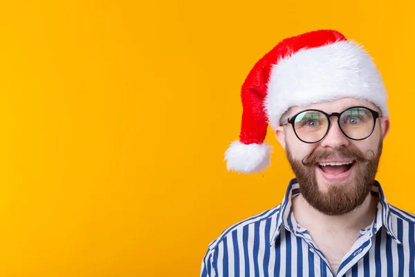 Joyeux fou mignon jeune hipster mâle en rouge santa claus chapeau posant sur fond jaune. Le concept de Noël et la nouvelle année. Espace publicitaire . — Photo