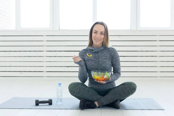 sport, healthy, people concept - Girl holding salad and dumbbell after fitness training