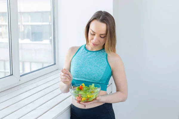 Stile di vita sano, fitness e dieta concetto - insalata alimentare e donna magra in abbigliamento sportivo vicino alla finestra — Foto Stock