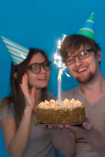 재미 괴상한 남자와 여자는 파란색 배경위에 스파클러와 생일 케이크를 들고 휴일 모자와 안경을 착용 — 스톡 사진