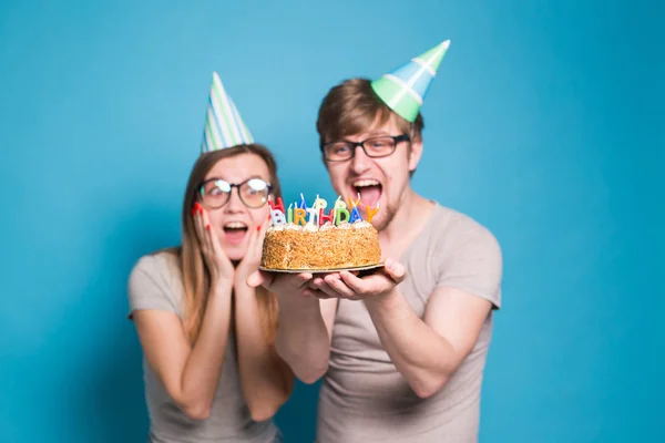재미 괴상한 남자와 여자는 파란색 배경위에 촛불과 생일 케이크를 들고 휴일 모자와 안경을 착용 — 스톡 사진