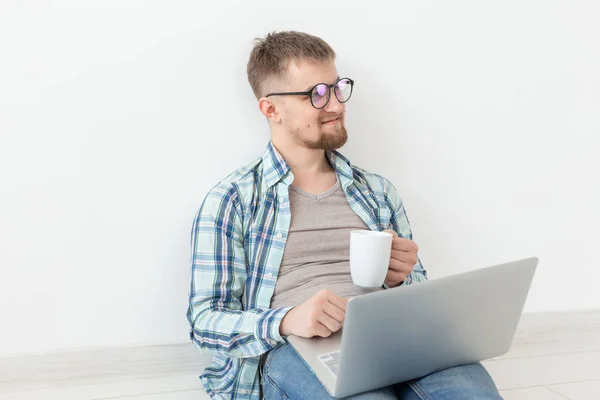 Θετικός νέος άντρας με casual ρούχα και γυαλιά να σερφάρει στο διαδίκτυο χρησιμοποιώντας Wi-Fi και ένα φορητό υπολογιστή σε αναζήτηση κατοικιών ενοικίασης. Σχέδιο οικιακής σίτισης και αναζήτησης διαμερισμάτων. — Φωτογραφία Αρχείου