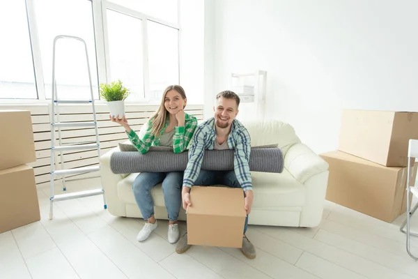 Jovem alegre alegre casal encantador menina e homem bonito segurando uma caixa com coisas e um pote com uma planta enquanto se muda para um novo apartamento. Conceito de habitação e hipoteca . — Fotografia de Stock