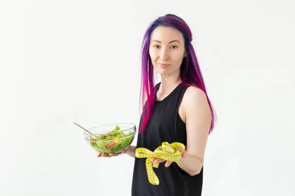 Молода азіатська дівчина хіпстер кольорове волосся тримає в руках вимірювальну стрічку і овочевий салат позує на білому тлі з копіспасом. Концепція здорового харчування . — стокове фото