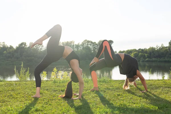 Armonía y concepto de estilo de vida saludable - Jóvenes mujeres delgadas en ropa deportiva practicando yoga al aire libre . —  Fotos de Stock