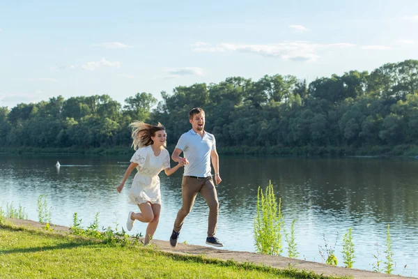 Liebes- und Beziehungskonzept - der glückliche Mann und die glückliche Frau beim Laufen in einem Park am See — Stockfoto