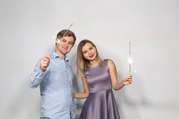 Festa, Ano Novo 2020, Natal e feriados conceito - jovem casal olhando para faíscas no fundo branco — Fotografia de Stock