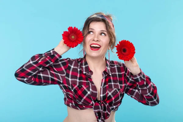 Ritratto ravvicinato di una bella giovane donna che tiene fiori rossi con cuori diversi nelle mani in posa su uno sfondo blu. Concetto di differenze e sfumature delicate . — Foto Stock