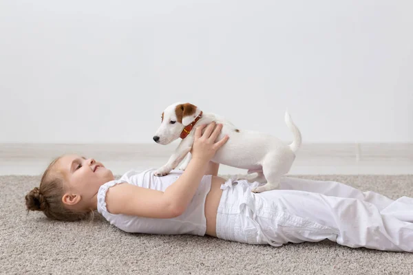 People, children and pets concept - little kid girl lying on the floor with cute puppy in hands — Stock Photo, Image