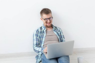 Rahat giysiler içinde Pozitif genç adam boş bir odada yerde oturan yeni konut arayışı içinde internette sörf. Internet ve dizüstü bilgisayar kullanarak bir daire bulma kavramı.