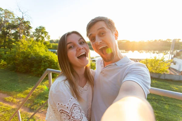 Schöne lustige romantische Paar auf Natur Hintergrund. attraktive junge Frau und schöner Mann machen Selfie, lächeln und schauen in die Kamera. — Stockfoto