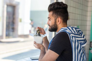 Yakışıklı genç hipster adam bir kafede oturan ve pencereye bakarak ahşap çubukları kullanarak Çin erişte yeme. Asya mutfağı konsepti.