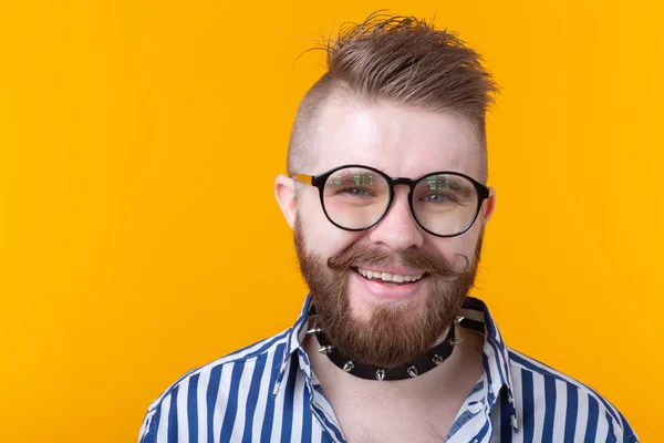 Jonge positieve trendy man hipster met een snor baard en Fetish ketting in shirt poseren op een gele achtergrond. Concept van Rock en subcultuur. — Stockfoto