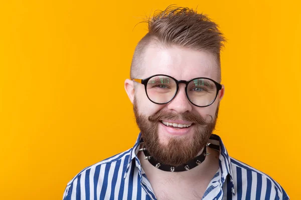 Joven hombre de moda positivo hipster con una barba bigote y collar fetiche en camisa posando sobre un fondo amarillo. Concepto de roca y subcultura . — Foto de Stock