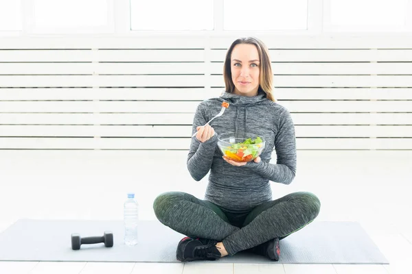 sport, healthy, people concept - Girl holding salad and dumbbell after fitness training