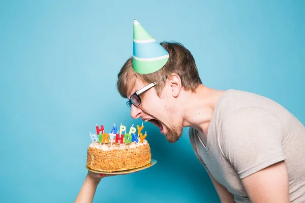 Vicces őrült fiatalember egy üdvözlőpapír kalap akar harapni le egy darab gratuláló torta. Fogalma bolondozás körül, és születésnapi üdvözletet. Lemezterület másolása — Stock Fotó
