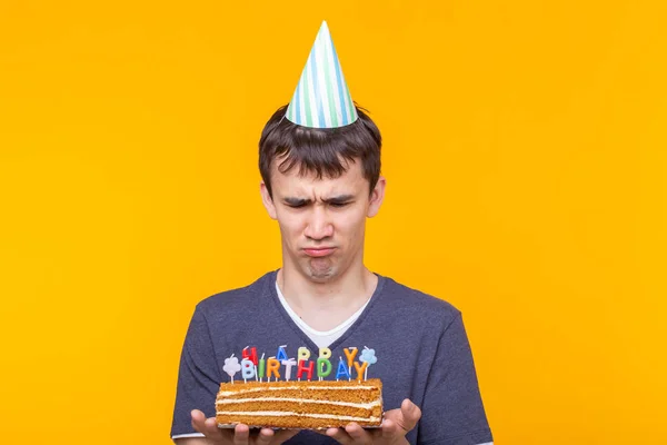 Vicces pozitív srác szemüveg tartja a kezében egy házi torta a felirat boldog születésnapot pózol a sárga háttér másolási tér. Az ünnepek és az évfordulók fogalma. — Stock Fotó