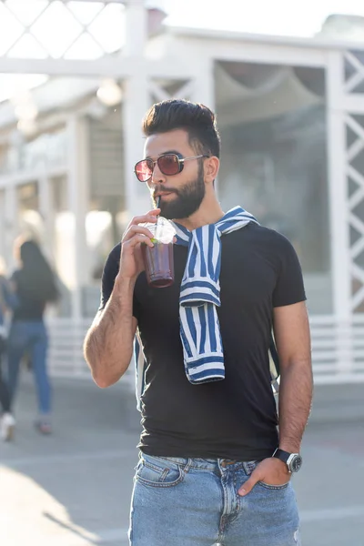 Schattig stijlvolle Arabische jonge mannelijke hipster met een snor en een baard en het dragen van glazen drinken sap met een rietje. Zomer vakantie concept. — Stockfoto