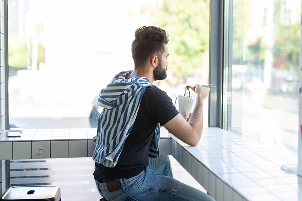 Portret przystojnego mężczyzny jedząc chińskie kluski w kawiarni i patrząc na okno. Koncepcja zdrowej kuchni azjatyckiej. — Zdjęcie stockowe