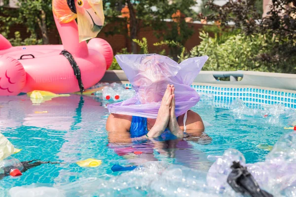 Ecology, plastic trash, environmental emergency and water pollution - desperate hoping man with a plastic bag over his head in a dirty swimming pool