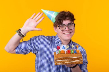 Elinde bir şapka ve sarı bir arka plan üzerinde poz bir ev yapımı kek ile Pozitif komik genç adam. Yıldönümü ve doğum günü konsepti.