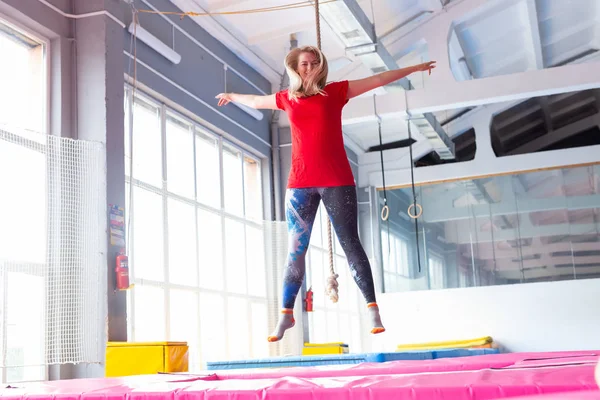 Fitness, diversión, ocio y deporte concepto de actividad - Mujer feliz joven saltando en un trampolín en el interior — Foto de Stock