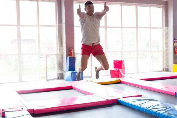 Fitness, diversão, lazer e esporte conceito de atividade - Bonito homem feliz pulando em um trampolim dentro de casa — Fotografia de Stock