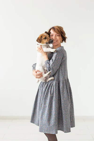 Encantadora joven sonriente con un elegante vestido gris sosteniendo a su perro favorito Jack Russell Terrier. Concepto perros favoritos . — Foto de Stock