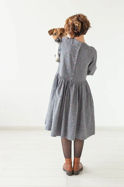 Ropa, diseñador, concepto de la gente - vista trasera de la mujer atractiva en un vestido gris posando en blanco con un perro — Foto de Stock
