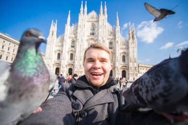 Kış seyahat, tatil ve kuşlar kavramı - selfie güvercinler yakınındaki Milan Katedrali Duomo di Milano, İtalya ile alarak genç komik adam.