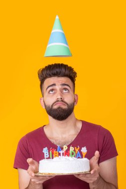Sarı bir arka plan üzerinde poz yazıt mutlu doğum günü ile kutlama pastası tutan bordo t-shirt Pozitif yakışıklı genç hipster adam. Tebrikler ve yıldönümleri kavramı.