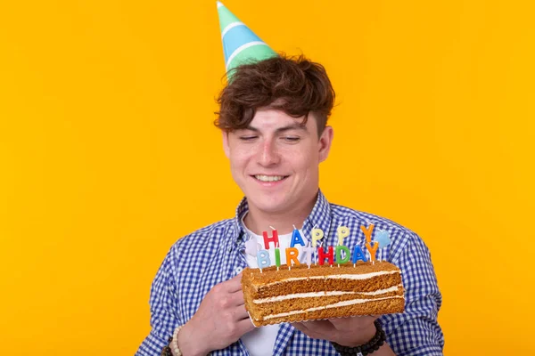 Jovem engraçado positivo com um boné e um bolo caseiro em suas mãos posando em um fundo amarelo. Aniversário e conceito de aniversário . — Fotografia de Stock