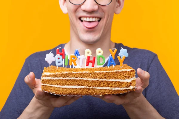 Crazy glad ung man i glas och Paper gratulatoriska hattar hålla tårtor Grattis på födelsedagen stående på en gul bakgrund. Jubileums gratulationer koncept. — Stockfoto