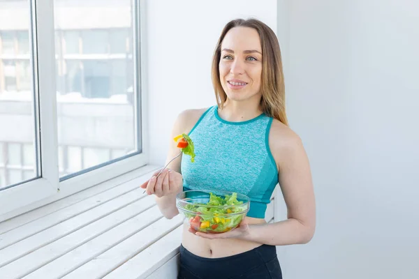 Stile di vita sano, fitness e dieta concetto - insalata alimentare e donna magra in abbigliamento sportivo vicino alla finestra — Foto Stock