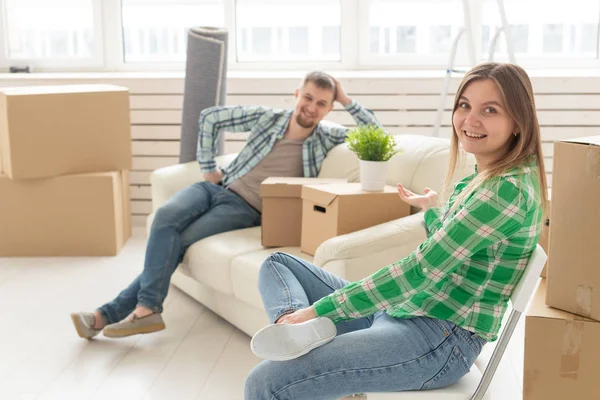 Позитивная веселая пара радуется переезду своей новой квартиры, сидя в гостиной с вещами. Концепция новоселья и ипотеки для молодой семьи . — стоковое фото