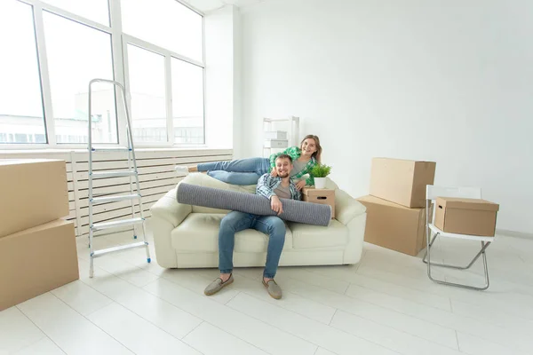 Веселая молодая пара радуется переезду в новый дом, раскладывая свои вещи в гостиной. Концепция новоселья и ипотеки для молодой семьи — стоковое фото