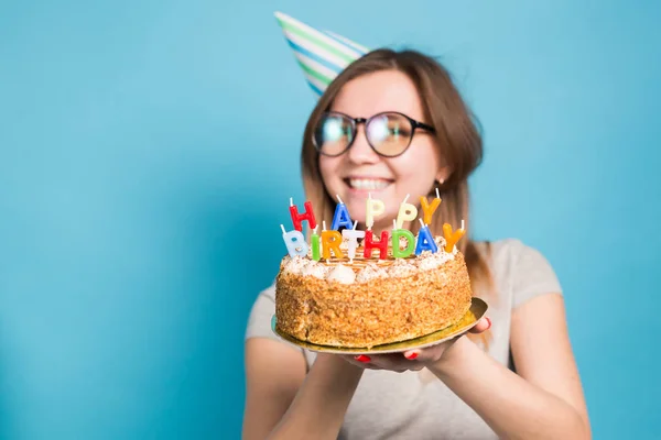 파란색 배경에 서 그녀의 손에 생일 케이크를 들고 축하 종이 모자에 매력적인 메리 미친 어린 소녀 학생. 광고 공간. — 스톡 사진