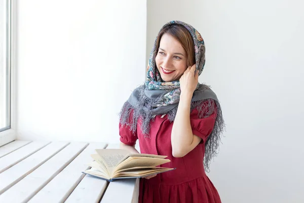 Retrato de close-up de uma jovem mulher de sonho bonito com um livro na mão olhando pela janela e pensando em algo. Concept amantes de clássicos e literatura . — Fotografia de Stock