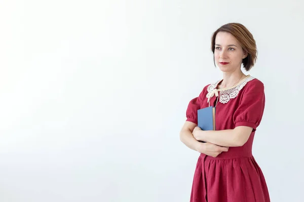 Portrait of cute smiling modest woman in dress holding classic book in hands on white background. Concept of lovers of history and classics. Copy space