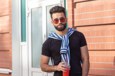 Bir bıyık ve sakal ve bir saman ile meyve suyu içme gözlük giyen sevimli şık Arap genç erkek hipster. Yaz tatili konsepti.