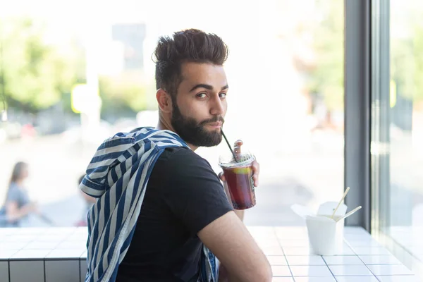 Retrato de un hombre árabe guapo bebiendo batido en un café. El concepto de bebidas saludables y estilo de vida . — Foto de Stock