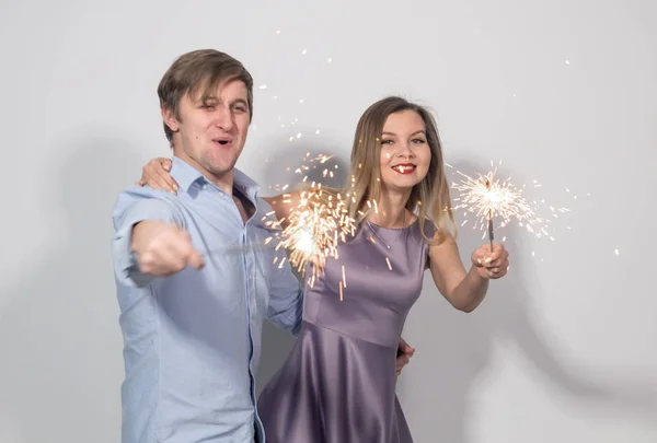 Feriados, Ano Novo, Natal, festa e celebrações conceito - jovem casal com brilhos no fundo branco — Fotografia de Stock