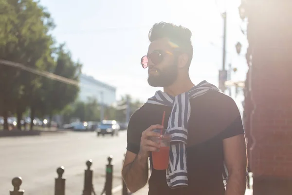 Portret van een positieve vrolijke jonge Arabische man met een glas sap met een rietje tijdens het wandelen in de stad op een warme zonnige zomerdag. Het concept van rust na studie en werk in het weekend. — Stockfoto