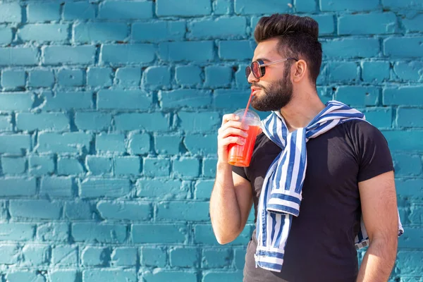 Lindo estilo árabe joven hipster masculino con un bigote y una barba y el uso de gafas de beber jugo con una paja. Concepto vacaciones de verano . — Foto de Stock
