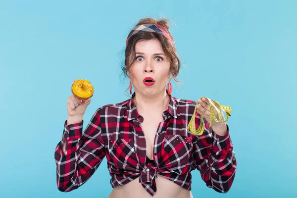 다이어트, 체중 감량 및 정크 푸드 - 파란색 배경 위에 디저트와 측정 테이프 중에서 선택하는 핀 업 여성 — 스톡 사진