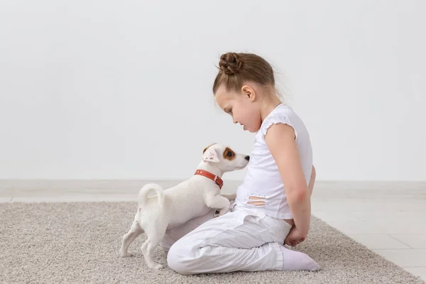 Gente, mascotas y concepto animal - Niña sentada en el suelo sobre fondo blanco y sosteniendo al cachorro Jack Russell Terrier — Foto de Stock