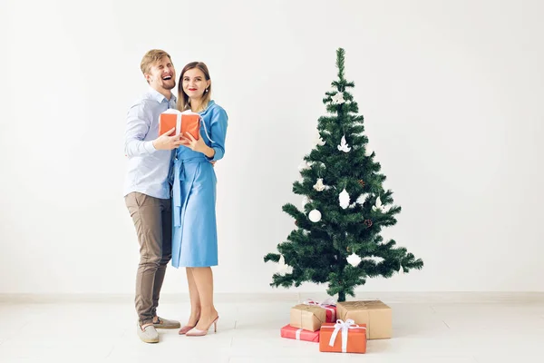 Concepto de fiestas y celebraciones - Linda pareja joven intercambiando regalos de Navidad frente a un árbol de Navidad — Foto de Stock