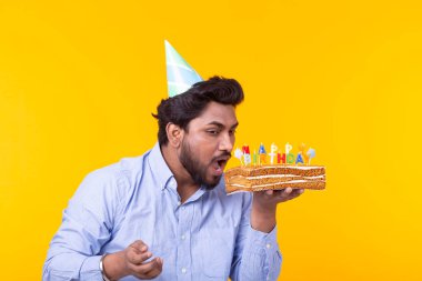 Elinde bir şapka ve sarı bir arka plan üzerinde poz bir ev yapımı kek ile Pozitif komik genç hintli adam. Yıldönümü ve doğum günü konsepti.