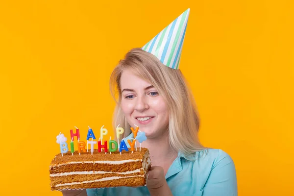 Ünnepek és fél cocept-pozitív fiatal nő, aki egy boldog születésnapi torta pózol egy sárga háttér. — Stock Fotó